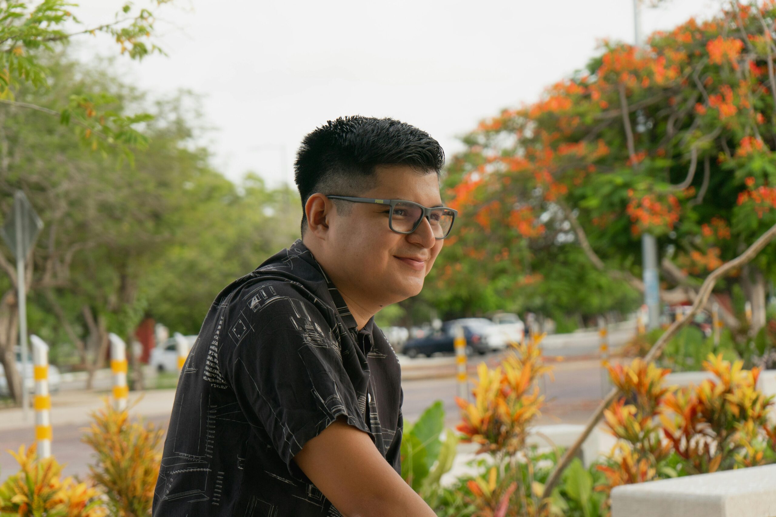 Portrait of a man with glasses smiling in a vibrant park setting in Merida, Yucatan, Mexico.